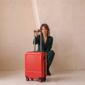 Frau im grünen Jumpsuit mit rotem -Rollen Carry On von NeoGo